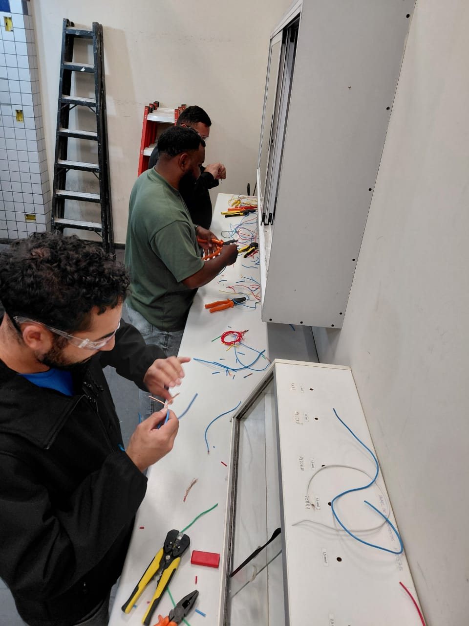 Aula prática de fiação elétrica em bancada, parte da formação de mão de obra qualificada da Emccamp