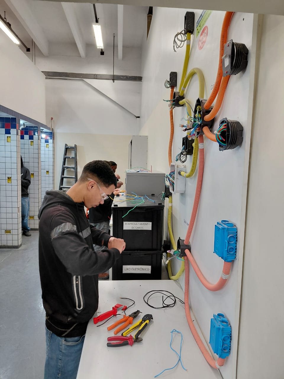 Turma da Emccamp em bancada de treinamento de instalações elétricas, formação de mão de obra qualificada